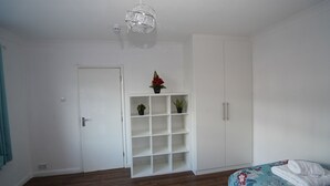 Un dormitorio con cama, armario, estante con plantas y una puerta.