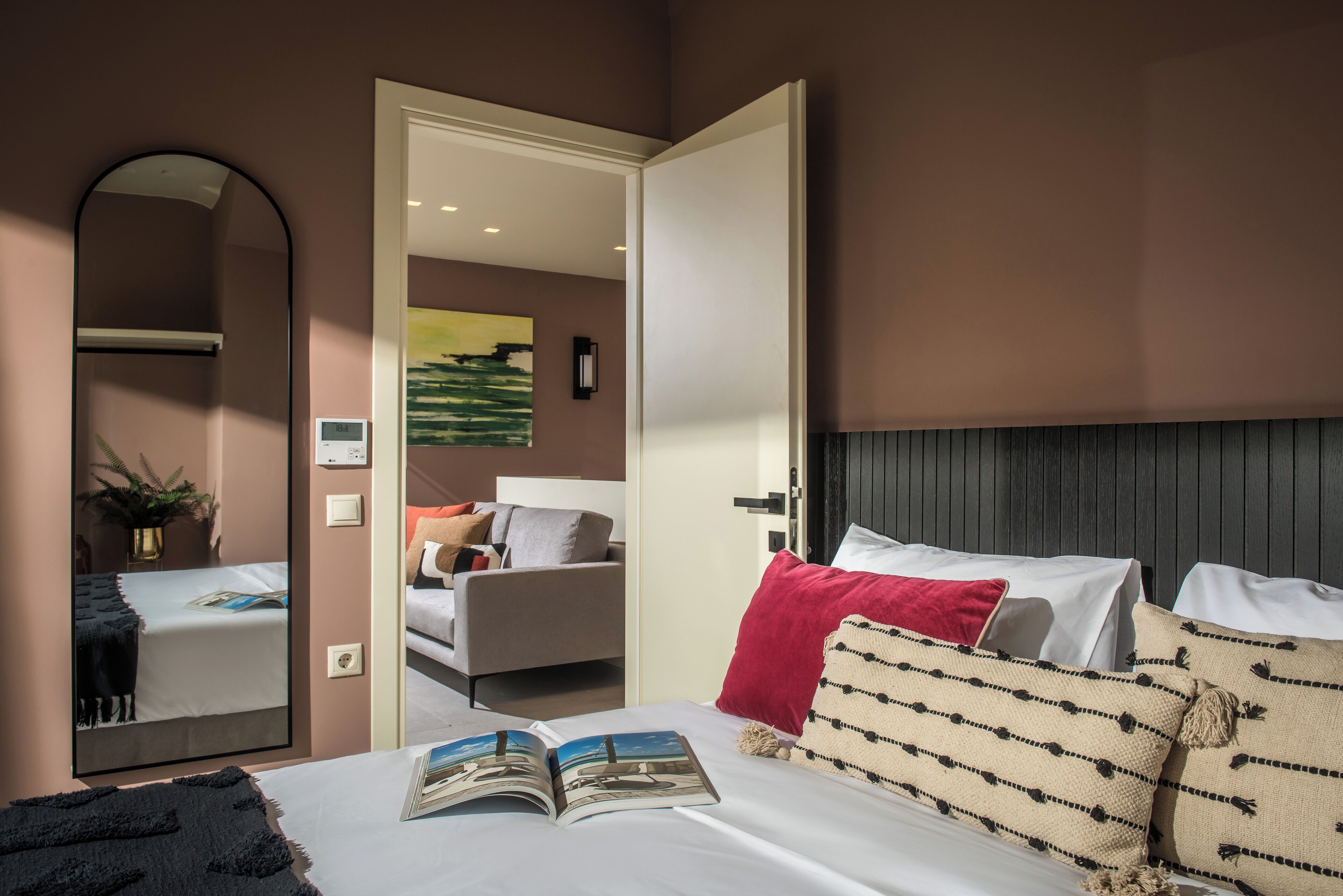 A modern hotel room with a large bed, a sitting area with a sofa, a dining table, and a large mirror.