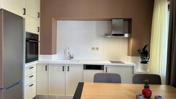 A modern kitchen with white cabinets, a built-in oven, a stainless steel range hood, and a dining area with a wooden table and chairs.