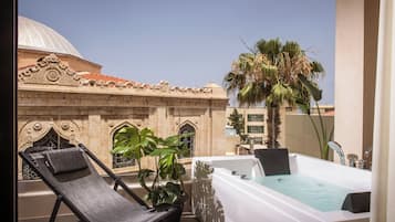 A balcony with a sun lounger, a hot tub, and a large potted plant.