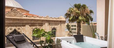 A balcony with a sun lounger, a hot tub, and a large potted plant.