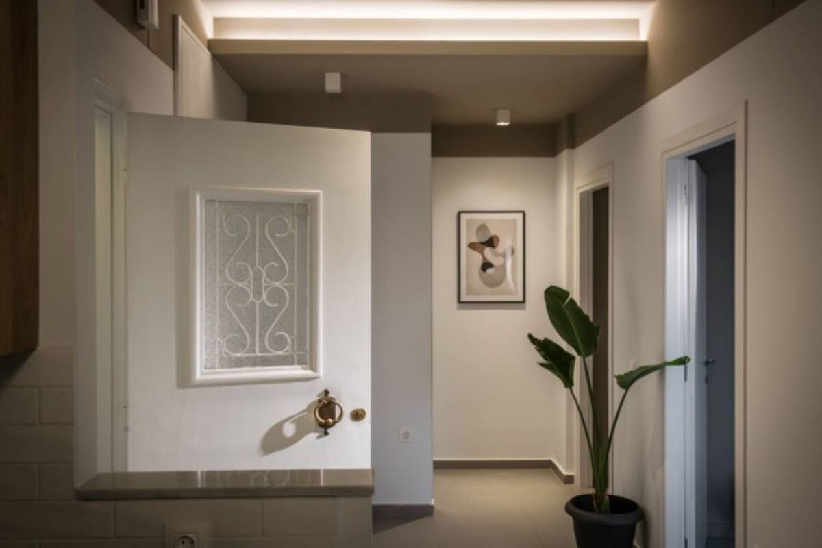 Um corredor com uma porta branca, uma obra de arte emoldurada e um vaso de planta.