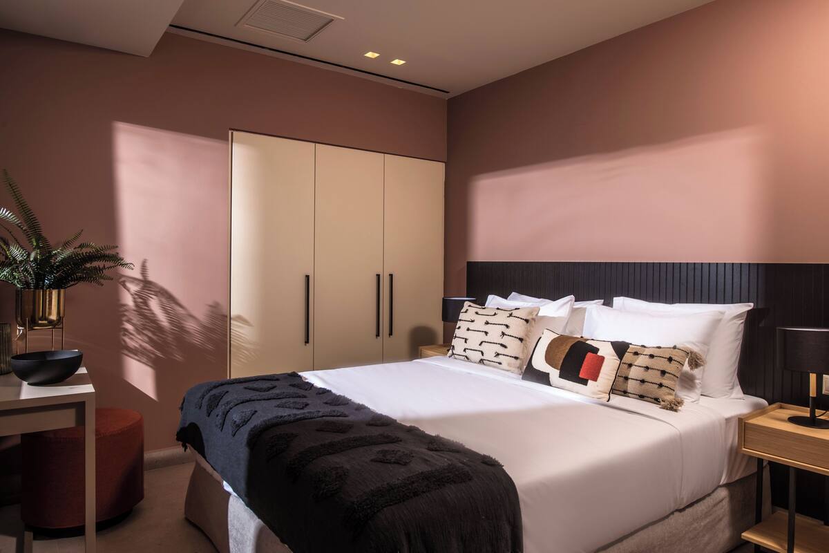 Quarto moderno com uma cama grande, mesas de cabeceira, um guarda-roupa e uma escrivaninha com uma planta.