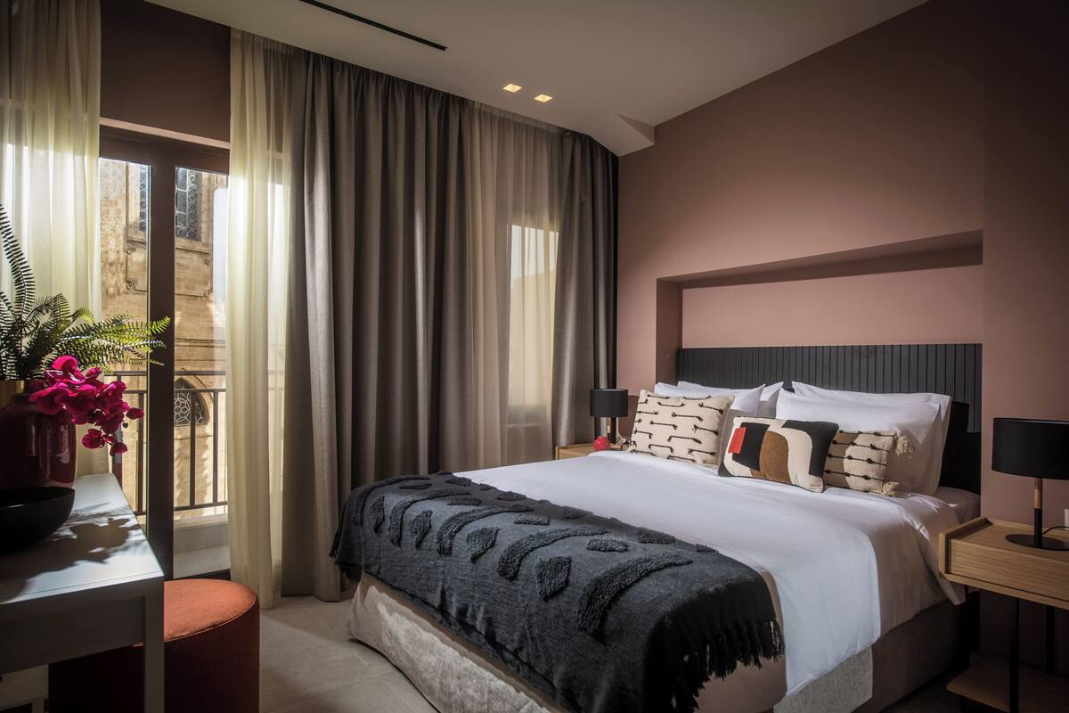 Quarto de hotel moderno com uma cama grande, uma mesinha de cabeceira e vista para a varanda externa.