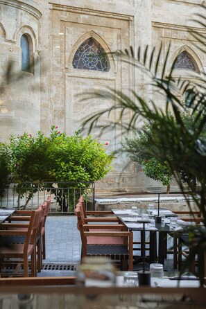 An outdoor seating area with tables and chairs, a stone building with arched windows, and a small tree in the foreground. - Centro Vero Suites by Omilos Hotels (Heraklion)