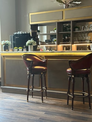 Angolo bar con due poltrone in pelle, una macchina per il caffè ed scaffali con bicchieri.