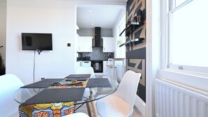 A modern kitchen with white cabinets, a black range hood, and a window with blinds. - Close to Tube - Free Parking - Pet Friendly (London)