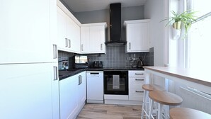 A modern kitchen with white cabinets, a black range hood, and a wooden countertop. - Close to Tube - Free Parking - Pet Friendly (London)