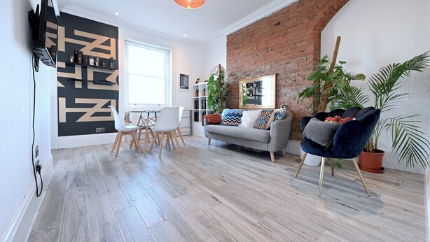 A modern living room with a grey sofa, a blue armchair, and a dining area with white chairs. - Close to Tube - Free Parking - Pet Friendly (London)