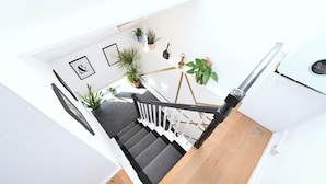 A staircase with a wooden finish, white walls, and black railings. There are several potted plants on the landing. - Close to Tube - Free Parking - Pet Friendly (London)