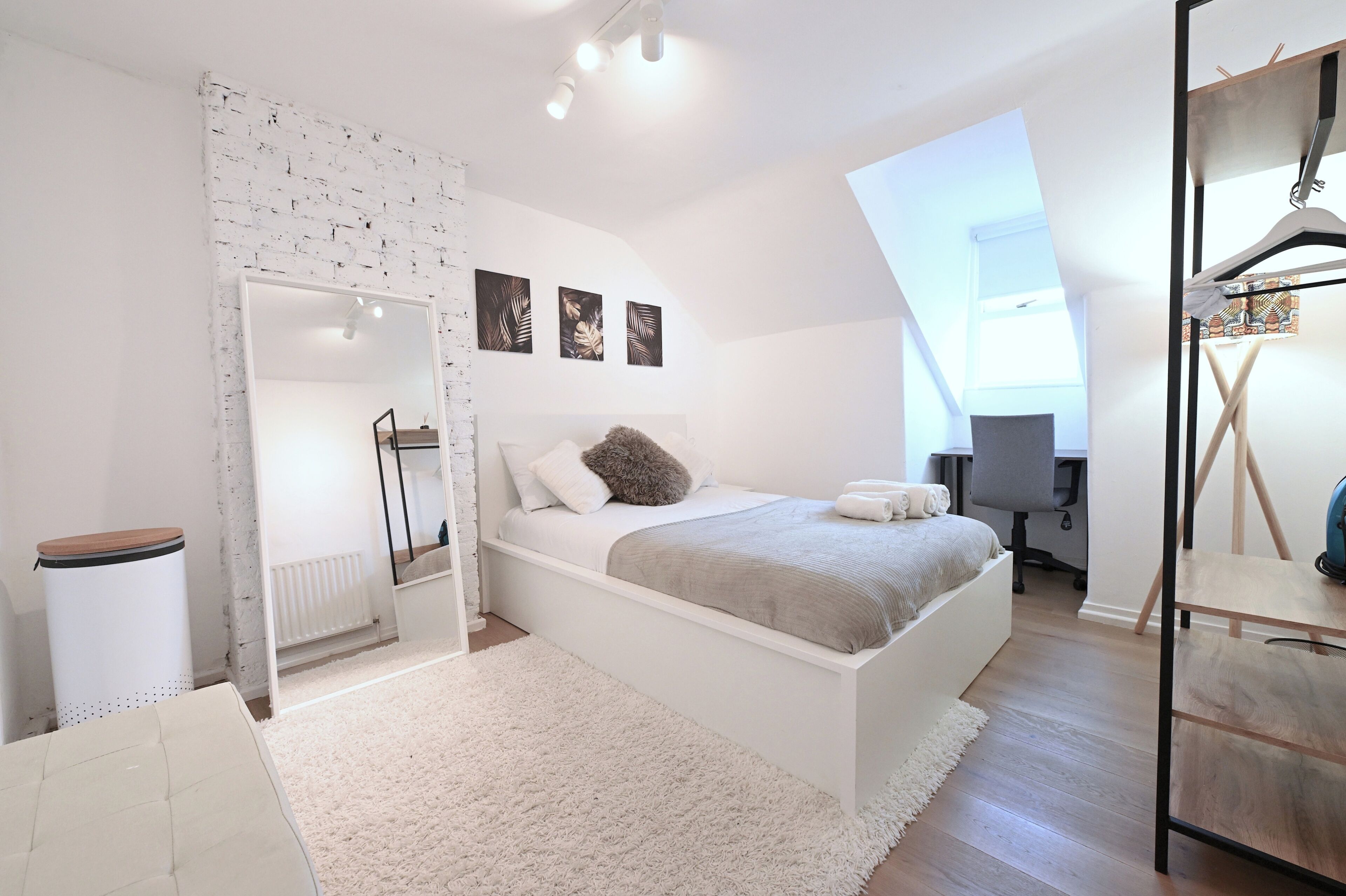 Une chambre moderne avec un lit blanc, un grand miroir, un radiateur et un bureau avec une chaise.