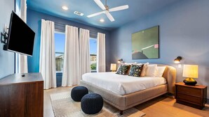 Un dormitorio moderno con cama, televisor, ventilador de techo y vistas al exterior.