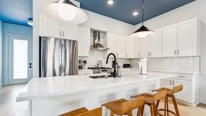 Una cocina moderna con armarios blancos, electrodomésticos de acero inoxidable y taburetes de bar de madera.