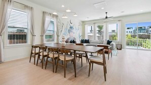 Uma sala de estar espaçosa com uma mesa de jantar grande, assentos confortáveis e vista para o bairro.