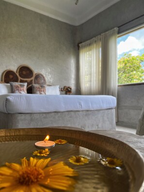 A bedroom with a bed, pillows, a bedside table with a candle, and a window with curtains. - Matsya Island Retreat (Port Blair)