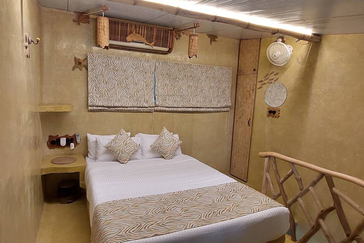 Um quarto com cama, mesa de cabeceira, ventoinha na parede e decoração na parede.