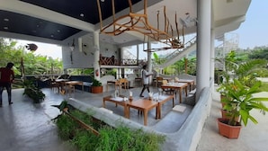 Een openluchtrestaurant met houten tafels en stoelen, omgeven door groen en een modern architectonisch ontwerp.