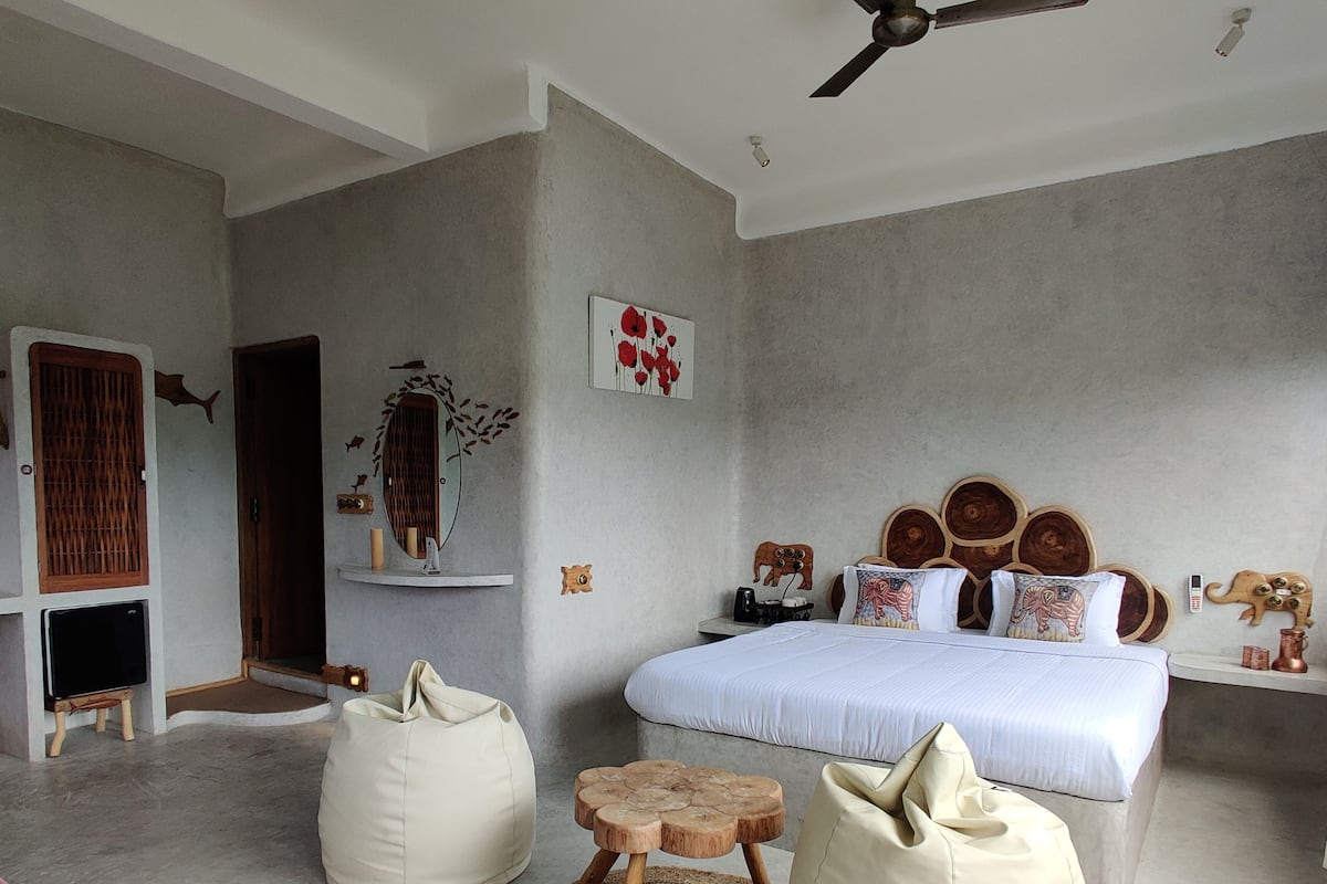 Quarto com cama, ventoinha no teto, mesa de cabeceira e espelho fixado na parede.