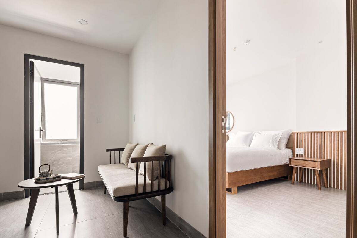 Une chambre moderne avec un lit en bois, une petite table de chevet, une chaise et une table sur laquelle se trouvent un panier et un livre.