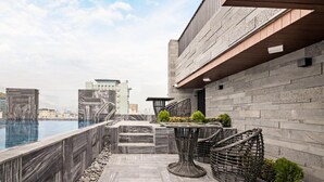 Una terrazza sul tetto con piscina, scale in pietra, mobili in vimini e vista sulla città.