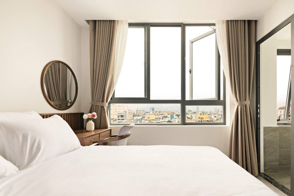 Une chambre d’hôtel avec un lit, une table de chevet, un miroir et une fenêtre avec des rideaux.