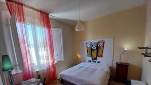 Une chambre à coucher avec un lit, un bureau recouvert de papiers, une lampe, une chaise, une fenêtre avec des rideaux rouges et une affiche accrochée au mur.