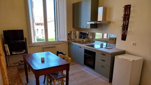 Une cuisine compacte comprenant une table à manger, des chaises, un four encastré, un réfrigérateur et une fenêtre laissant entrer la lumière naturelle.