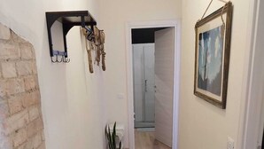 Un couloir avec un mur en briques, un plancher en bois, une plante en pot, un porte-manteau et un tableau encadré accroché au mur.