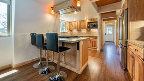 Una cocina moderna con armarios de madera, una isla central con taburetes altos y un refrigerador de acero inoxidable.