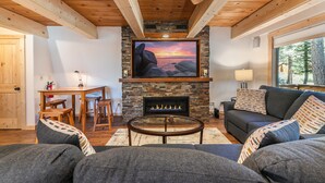 Una sala de estar acogedora con chimenea de piedra, vigas de madera en el techo, un sofá cómodo y un comedor con mesa y sillas.