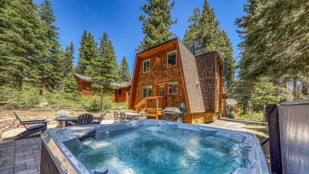 Una cabaña de madera con jacuzzi y zona de estar al aire libre, rodeada de árboles.