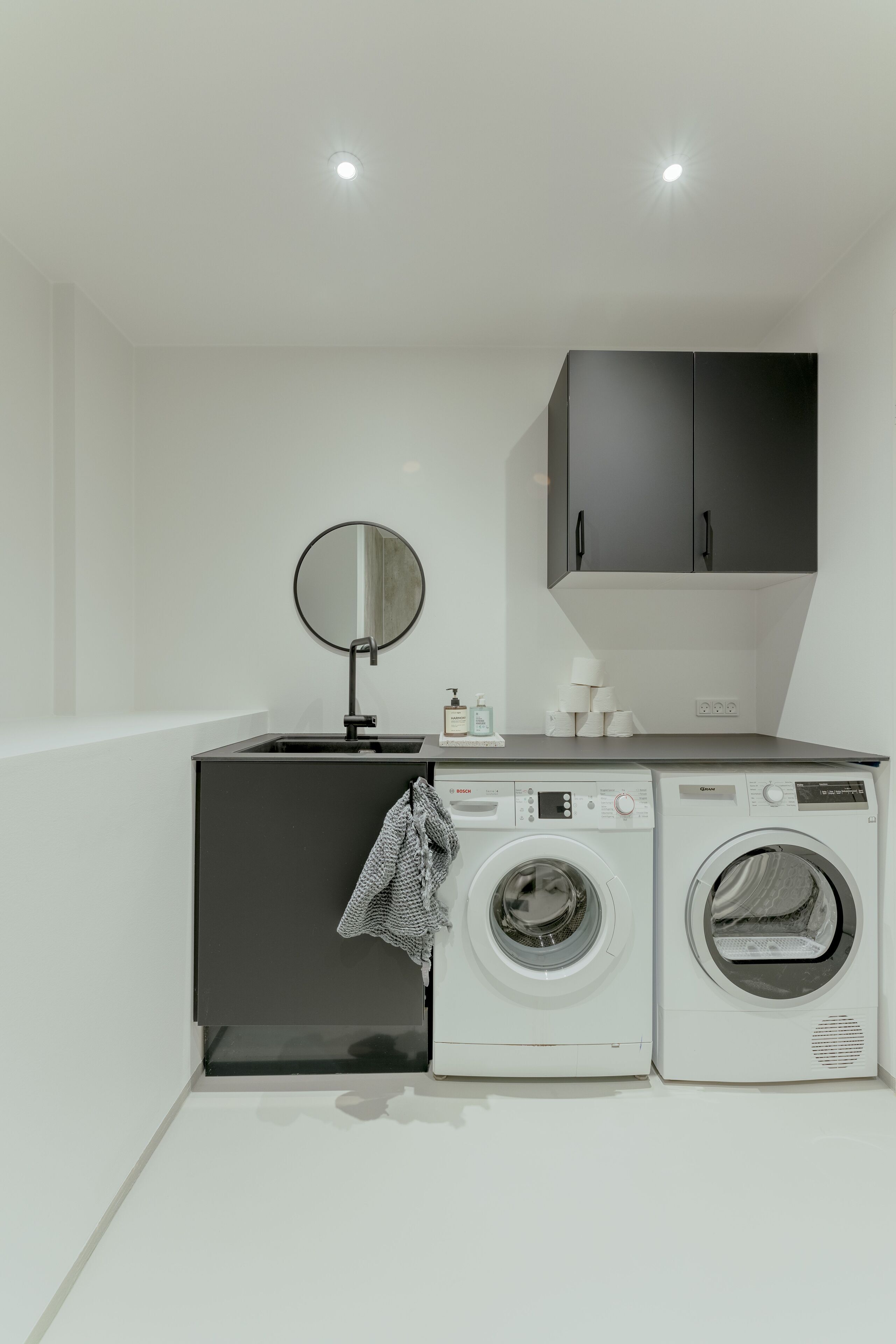 Un espace buanderie compact comprenant un lave-linge, un sèche-linge et un petit évier avec un miroir.