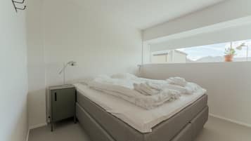 A bedroom with a bed, bedside table, lamp, and a window with a view of mountains.