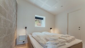 A modern bedroom with a large bed, a small window, and a built-in bedside table.