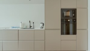 A modern kitchen with a built-in microwave and oven, a sink, and a kettle on the countertop.