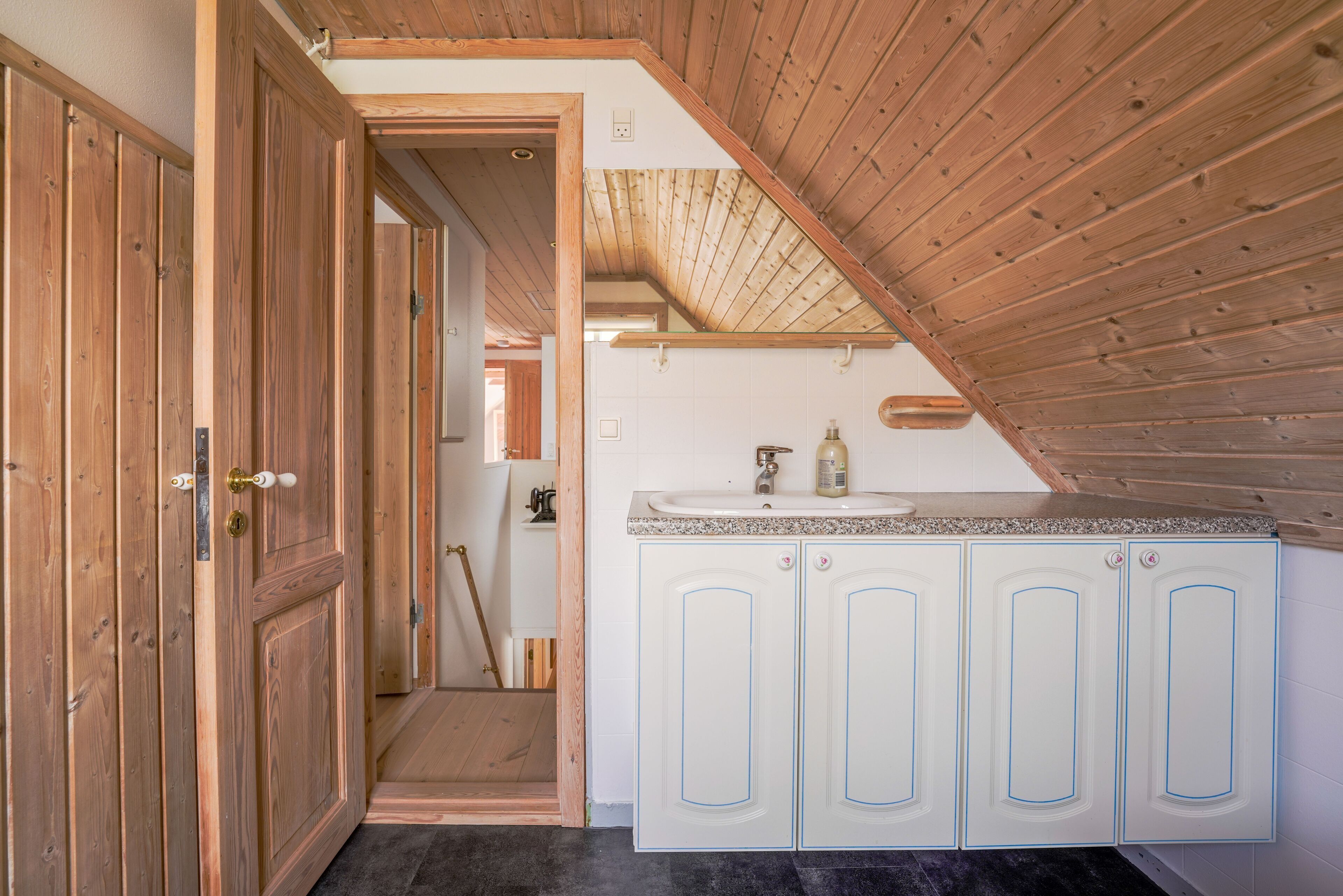 A wooden ceiling with a sloped design, white cabinets with blue trim, and a small sink area.