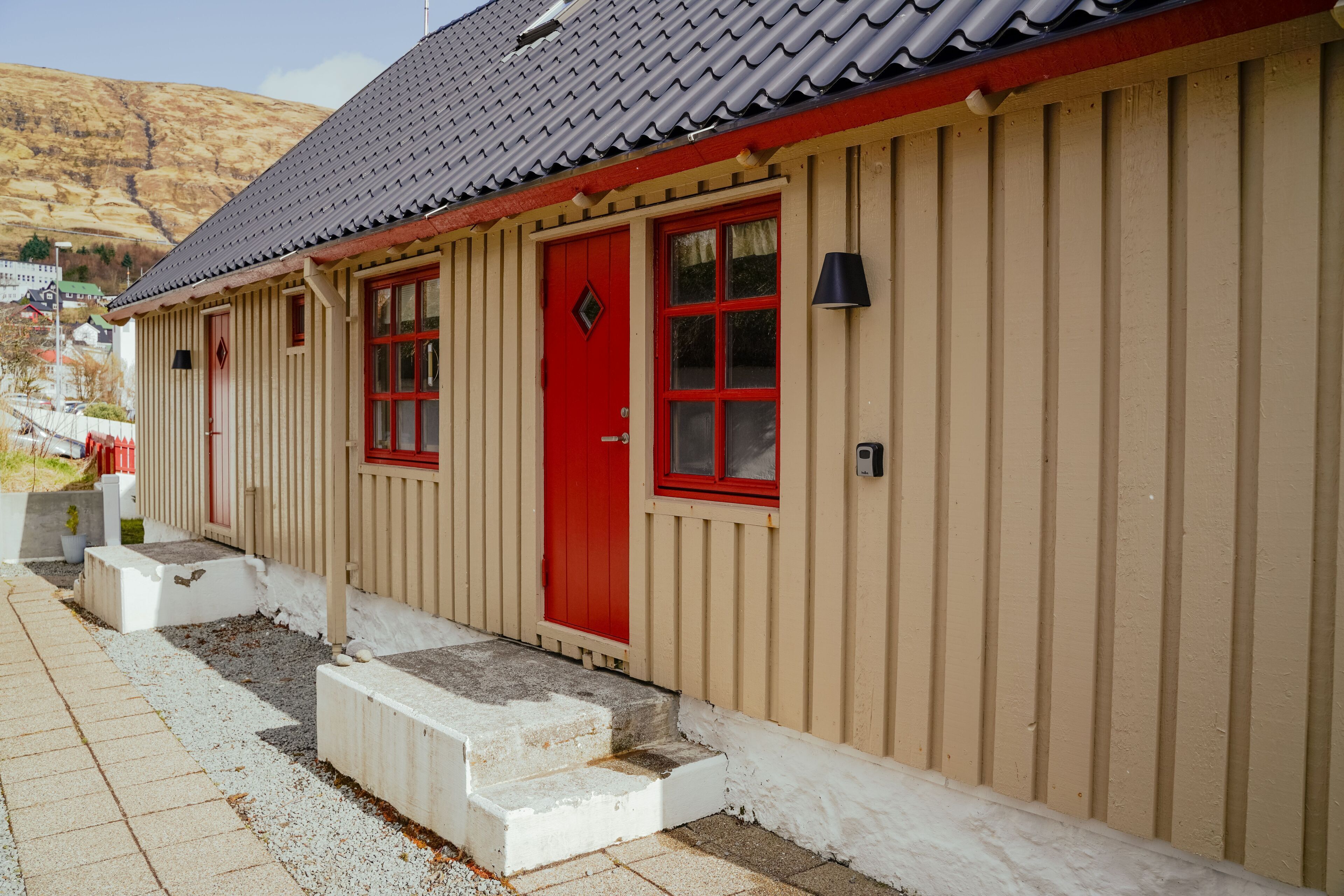 A building with a red door and windows, beige siding, and a grey roof.
