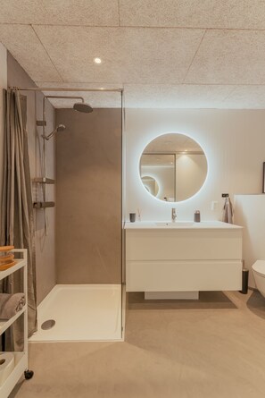 A modern bathroom with a glass-enclosed shower, a round mirror, and a white vanity. - Luxurious Waterfront Retreat | Spectacular Views (Vestmanna)