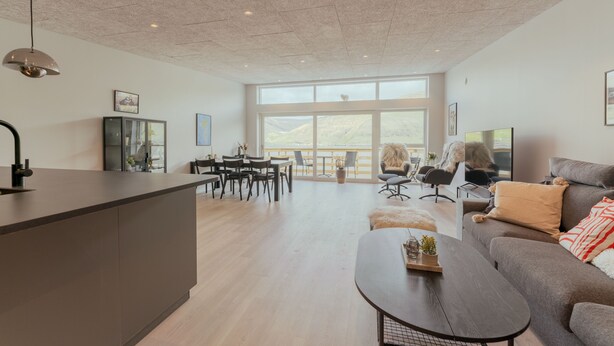A spacious living area with a large window, a dining area with chairs, a sofa, and a coffee table. - Luxurious Waterfront Retreat | Spectacular Views (Vestmanna)