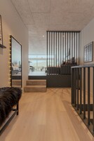 A modern interior with a wooden floor, a black bench, a staircase, and a view of the outdoors.