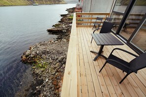 A wooden deck with a table and chairs overlooking a calm lake. - Luxurious Waterfront Retreat | Spectacular Views (Vestmanna)