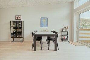 A modern dining area with a rectangular table, six chairs, a black metal cabinet, and a wall-mounted map. - Luxurious Waterfront Retreat | Spectacular Views (Vestmanna)