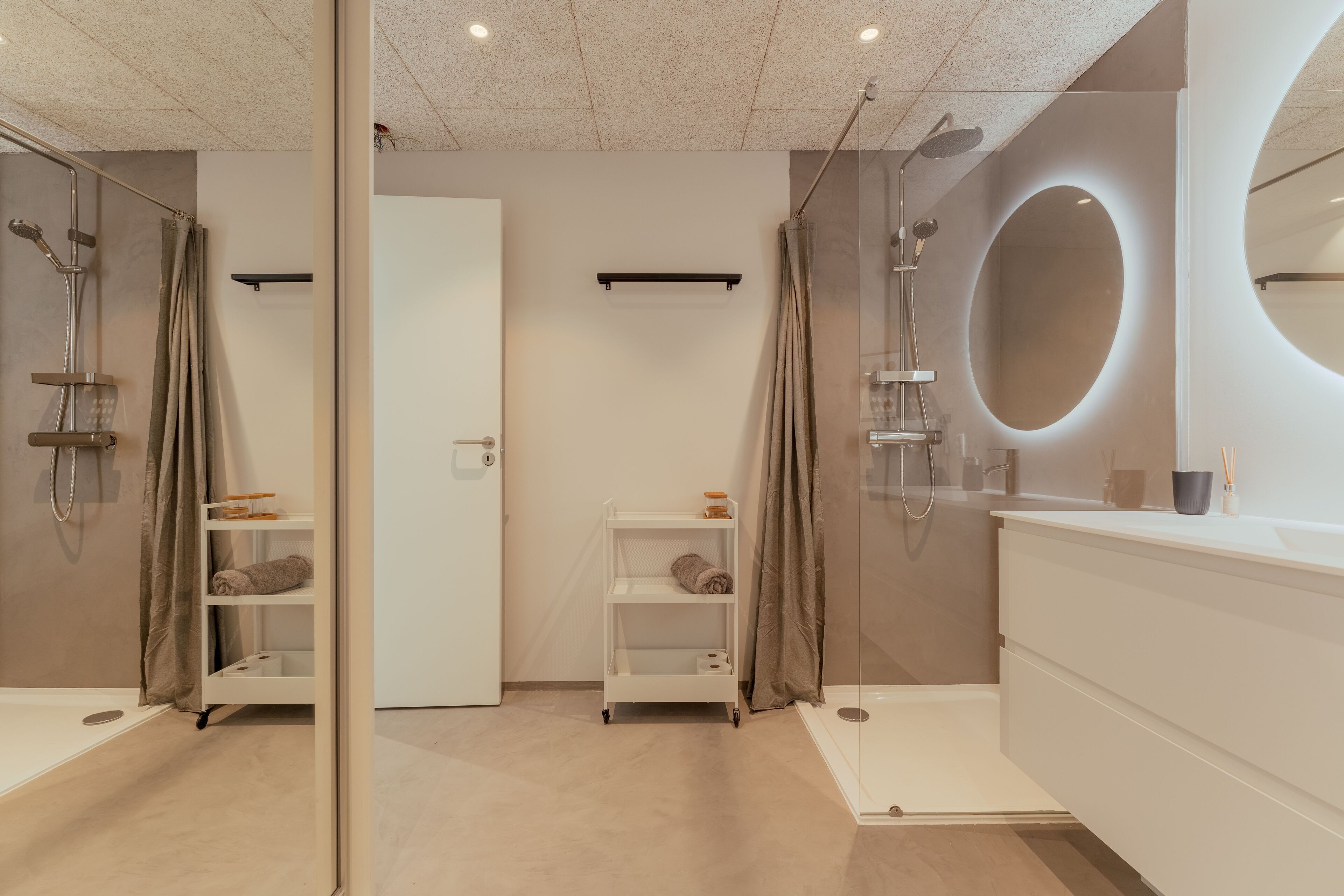 A modern bathroom with a glass shower enclosure, a white vanity with a round mirror, and a shelf with towels.