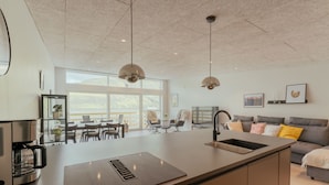 A modern kitchen with a central island, pendant lights, and a large window providing natural light. - Luxurious Waterfront Retreat | Spectacular Views (Vestmanna)