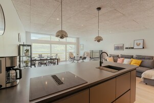 A modern kitchen with a central island, pendant lights, and a large window providing natural light.