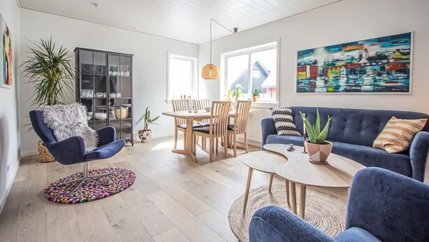 A modern living room with a blue sofa, a round coffee table, and a dining area with wooden chairs and a glass cabinet. - Lovely Apartment In The Heart Of Tórshavn (Tórshavn)