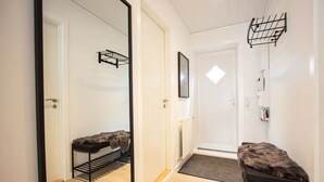 A hallway with a mirrored wardrobe, a fur-covered bench, a radiator, a door with a small window, and a black shelf on the wall. - Lovely Apartment In The Heart Of Tórshavn (Tórshavn)
