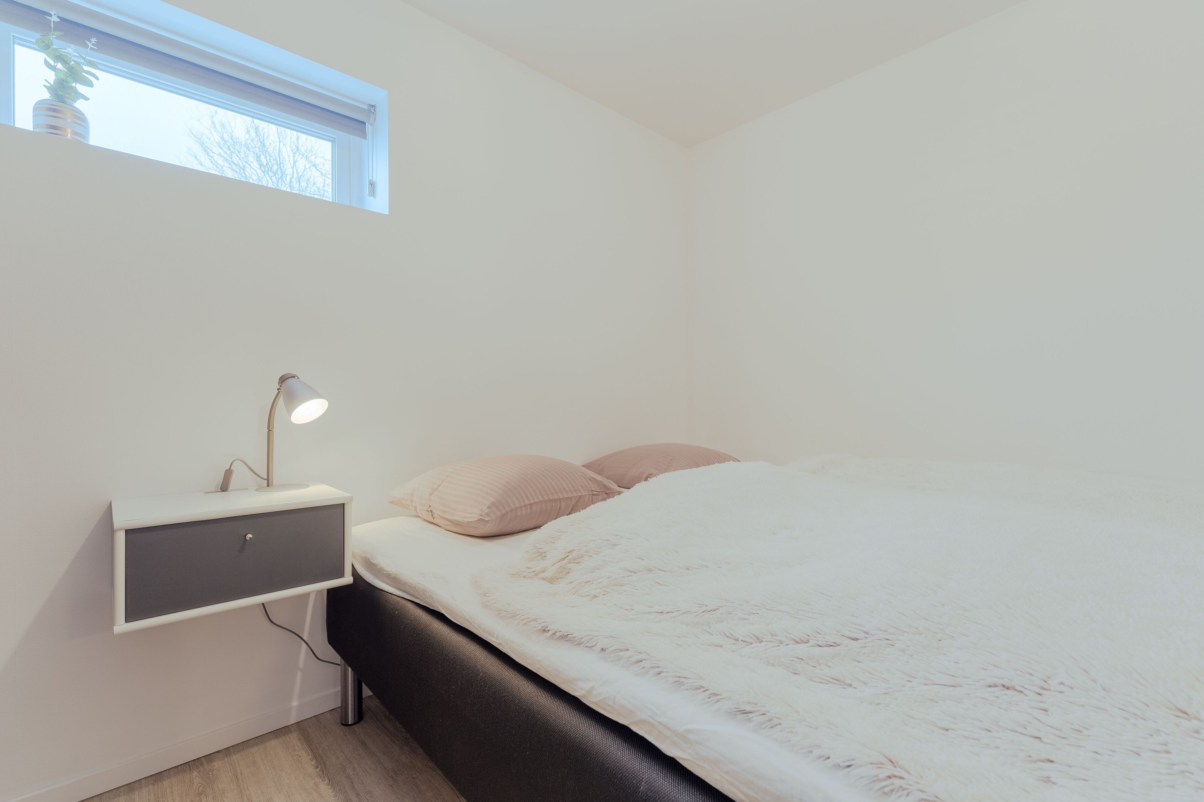 A bedroom with a bed, a bedside table with a lamp, and a window.