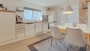 A modern kitchen with white cabinets, a built-in oven, and a dining area with a table and chairs.