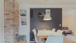 A modern dining area with a brick wall, a wooden table, white chairs, and a hanging pendant light.